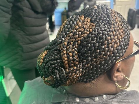 A close-up of an elegant braided updo with black and caramel highlights, showcasing intricate patterns against a vibrant blue backdrop.