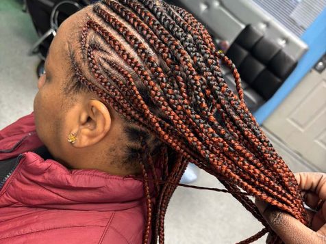 A close-up of intricate braided hair in black and red hues, styled by a hairdresser in a modern salon setting.
