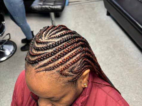 Close-up of a braided hairstyle featuring intricate cornrows with a mix of black and auburn strands, styled in a barbershop setting.