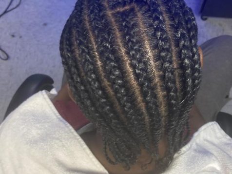 Close-up view of neatly braided hair with straight parting, draped in a white towel, seated in a salon with a blue background.