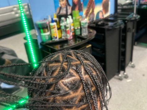 A close-up view of intricately braided hair in a salon, surrounded by hair products and colorful hairstyle posters on blue walls.