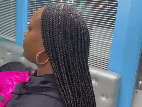 A person with long, black box braids sits in a brightly lit salon with modern decor and a window showcasing city lights.