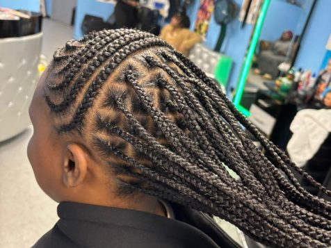 A close-up of braided hair in a salon, showcasing intricate cornrows styled elegantly, with colorful decor in the background.
